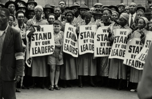 «Στεκόμαστε πλάι στους ηγέτες μας». Διαδήλωση μαύρων στο Γιοχάνεσμπουργκ το 1994, υποστηρικτική των προσπαθειών του Νέλσον Μαντέλα και του κόμματός του, του Αφρικανικού Εθνικού Κογκρέσου, να ελαχιστοποιήσουν τις συνέπειες του απαρτχάιντ, του φυλετικού διαχωρισμού που είχε επιβληθεί στη χώρα από τους λευκούς αποίκους και θεσμοθετήθηκε νομικά το 1948. Το απαρτχάιντ καταργήθηκε το 1991, αν και ακόμα και σήμερα επιβιώνουν ίχνη των συνεπειών του, ενώ στη χώρα έχουν προστεθεί πολλά καινούργια προβλήματα.  