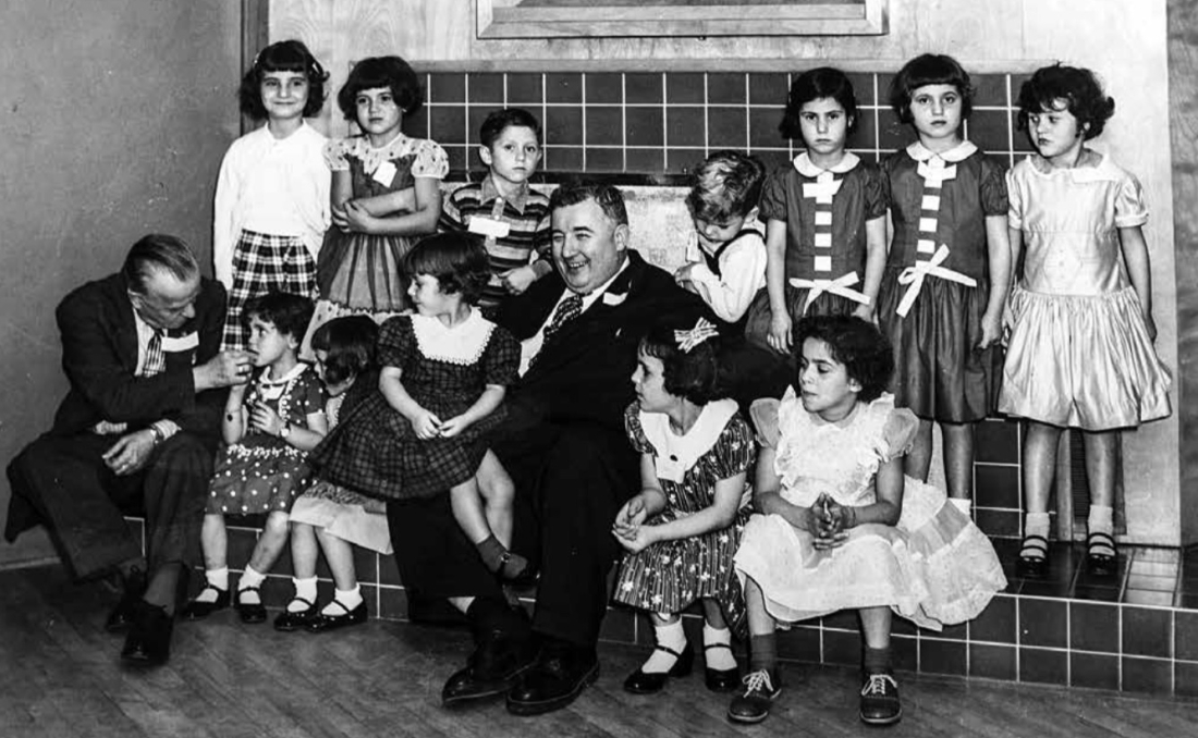 Ο Λίο Λάμπερσον της ΑΧΕΠΑ και, αριστερά, ο γερουσιαστής Ρόμπερτ Γουίλσον, περικυκλωμένοι από υιοθετημένα ελληνόπουλα σε πάρτι στο Σαν Ντιέγκο (φθινόπωρο 1956).  