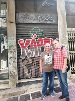 Ο Δημήτρης Κανελλόπουλος (δεξιά) συναντά τον περασμένο Ιούνιο τον Γιώργο Τσιλδερίκη έξω από το μαγαζί. Η μεγάλη φωτεινή επιγραφή έχει χάσει πλέον τα δυο πρώτα γράμματα, ενώ και το γκράφιτι στα ρολά μεγάλωσε και άπλωσε.