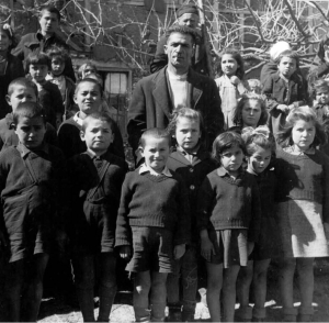 Μάρτιος 1947. Παιδιά από το χωριό Σκάφη της Κοζάνης που έχουν επιστρέψει στα σπίτια τους έπειτα από μια περίοδο παραμονής σε ξενώνα. Με το τσιγάρο στο στόμα, ο πρόεδρος του χωριού.  