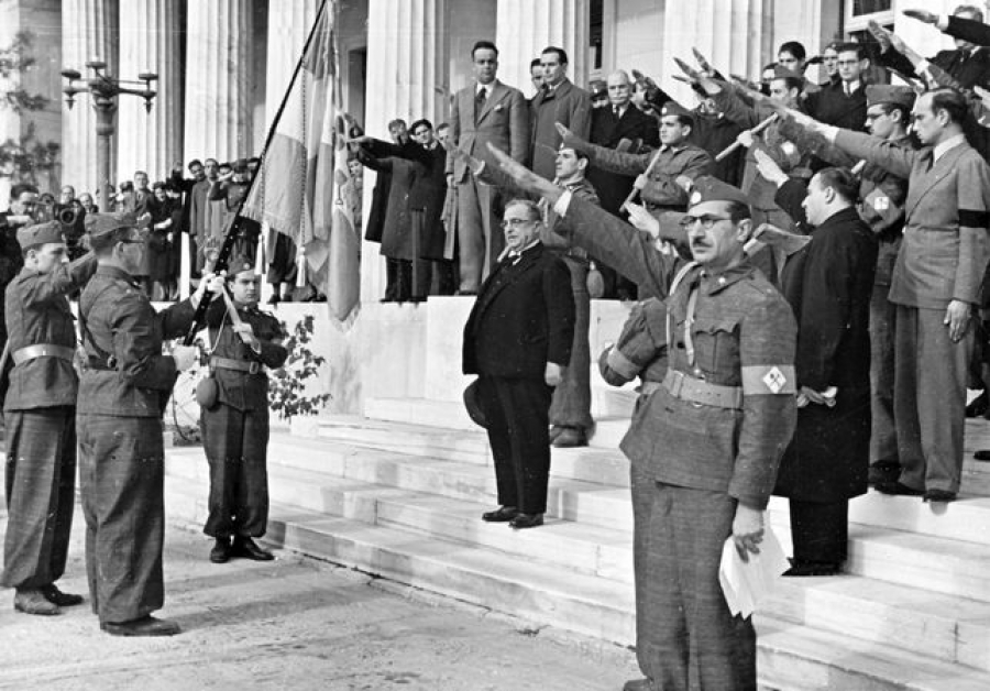 Ο Ιωάννης Μεταξάς, με το καπέλο του στο χέρι, σε στάση προσοχής στις σκάλες της Παλαιάς Βουλής, πιθανόν σε ανάκρουση Εθνικού Ύμνου. Οι παριστάμενοι αποδίδουν τον φασιστικό χαιρετισμό.  
