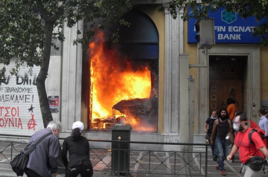 5 Μαΐου 2010. To κτίριο της Μαρφίν φλέγεται ενώ οι διαδηλωτές συνεχίζουν κανονικά την πορεία, σαν να μη συμβαίνει τίποτα. 