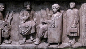 Δάσκαλος με δύο μαθητές και έναν νεαρό  ιματιοφύλακα (puer capsarius). Ανάγλυφο από το Neumagen, Trier Ρηνανίας (180-185 μ.Χ.).